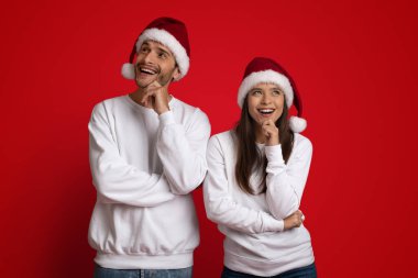 Düşünceli genç çift, Noel Baba şapkası takıyor. Kızıl Arkaplan 'ın üstünde bir şey düşünüyorlar.