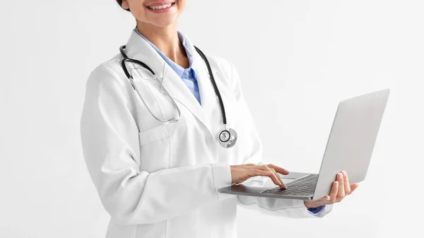 Przycięte młody indyjski lekarz pani w białym płaszczu z stetoskopem wpisując na komputerze na jasnym tle — Zdjęcie stockowe