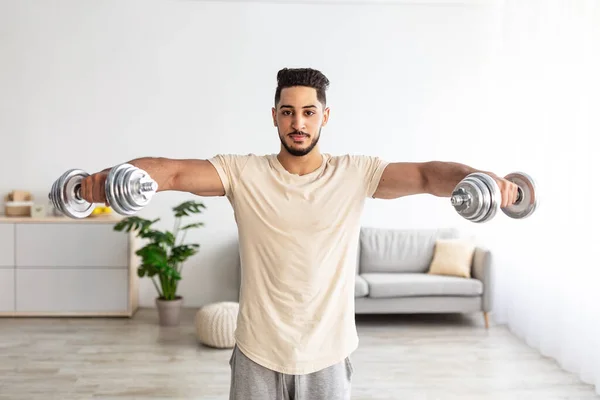 Portrait of fit young Arab guy pumping muscles, using dumbbells at home during coronavirus lockdown — 图库照片