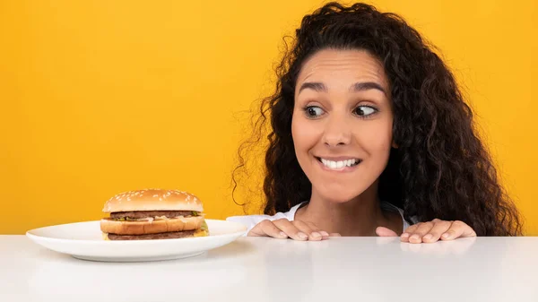 Éhes hölgy néz Burger kukucskál ki asztal — Stock Fotó