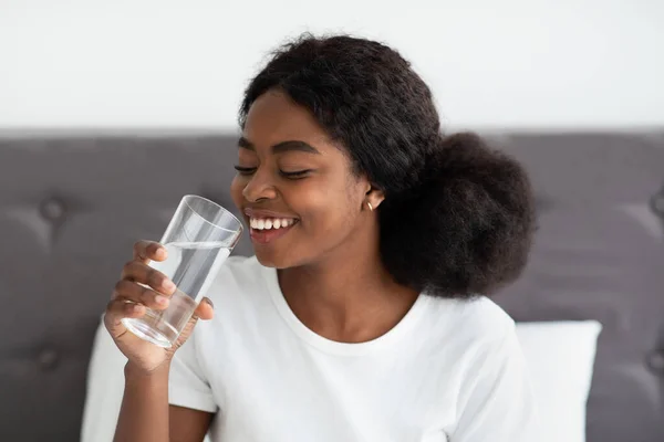 Felice giovane donna nera che beve acqua a letto — Foto Stock