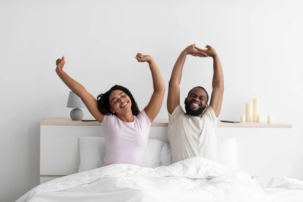 Щасливий тисячолітній чорний чоловік і дружина прокинулися, розтягуючи тіла на білому ліжку — стокове фото