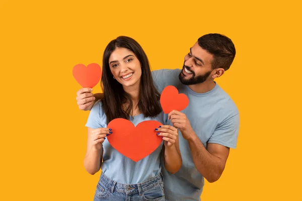 St. Alla hjärtans dag koncept. Glad kärleksfull mellanösternpar som håller röda valentiner kort och omfamnar — Stockfoto