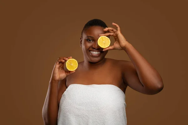 Plus size black woman covering eye with halves of citrus — Stock Photo, Image