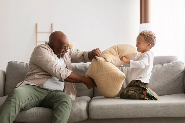 Vovô preto e pequeno neto tendo travesseiro luta em casa — Fotografia de Stock