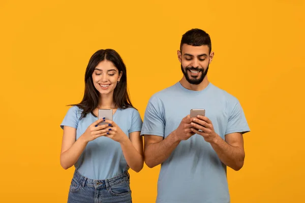 Jeune couple moyen-oriental tenant leurs smartphones et jouer au jeu ou bavarder en ligne, fond jaune — Photo