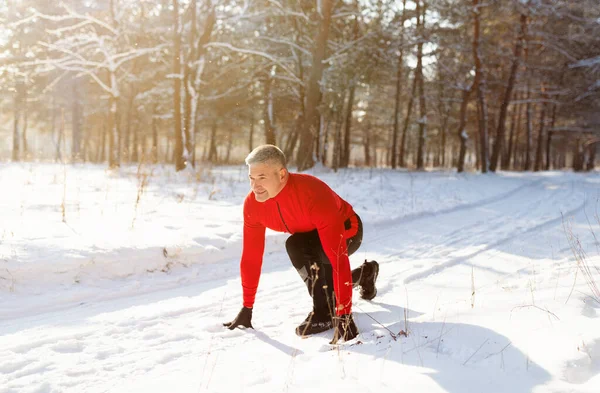 Alegre hombre mayor listo para correr en el camino nevado del campo en el frío día de invierno, longitud completa. Concepto de estilo activo —  Fotos de Stock