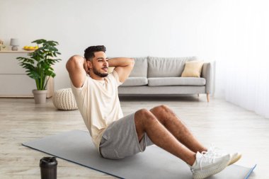 Spor yapan genç bir Arap, karın kası egzersizi yapıyor, evde çalışıyor, boy boy portresi yapıyor.