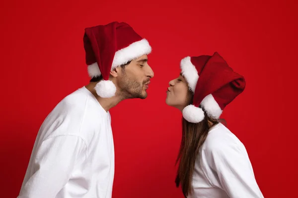 Beso de Navidad. hombre y mujer en santa sombreros besos sobre rojo fondo — Foto de Stock