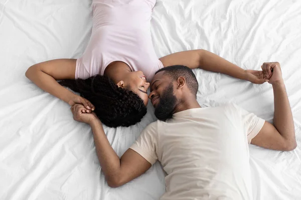 Boldog nyugodt fiatal fekete férj és feleség élvezze a gyengéd pillanatot együtt, feküdjön a fehér ágyon — Stock Fotó
