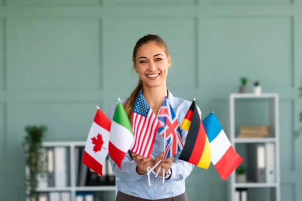 Tutor feminino feliz mostrando um monte de bandeiras diversas, recomendando língua estrangeira estudando escola — Fotografia de Stock