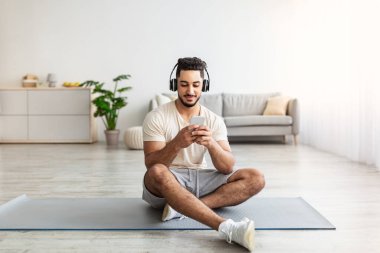 Kulaklıklı genç bir Arap evdeki cep telefonuyla yaptığı antreman için müzik listesi seçiyor.