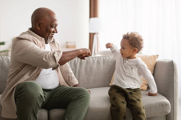 Feliz avô negro e pequeno neto batendo punhos em casa — Fotografia de Stock