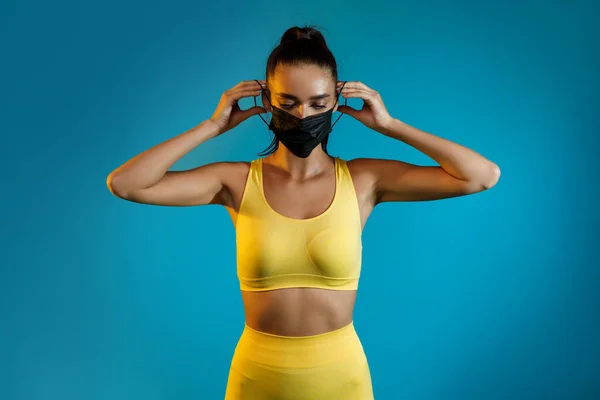 Sporty Woman Putting On Face Mask Standing On Blue Background — Stock Photo, Image