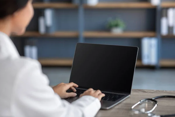 Giovane medico donna indiana in camice bianco digitando sul computer con schermo vuoto all'interno dell'ufficio — Foto Stock