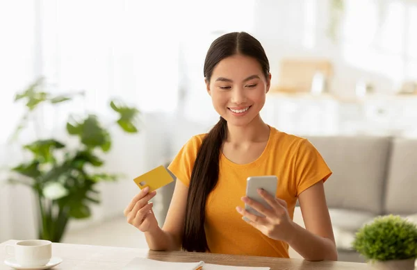 Easy contactless payment. Happy korean lady making purchases via internet, using smartphone and holding credit card — Stock Photo, Image