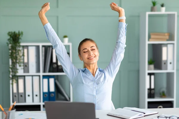 Stressverlichting. Vrouwelijke kantoormedewerker die handen uitstrekt met gesloten ogen tijdens het werken op laptop, zittend op de werkplek — Stockfoto