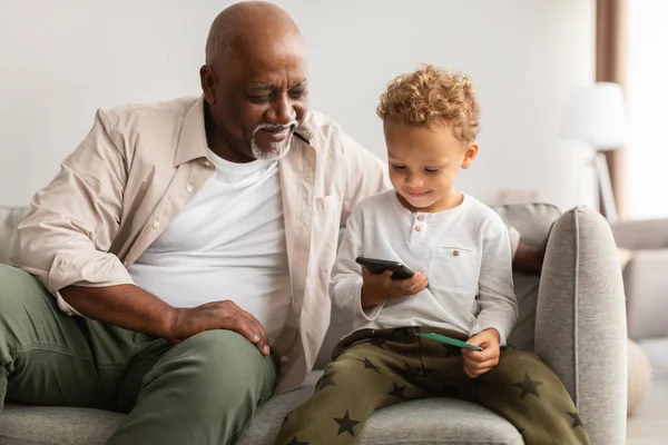 Avô preto e neto usando celular juntos em casa — Fotografia de Stock