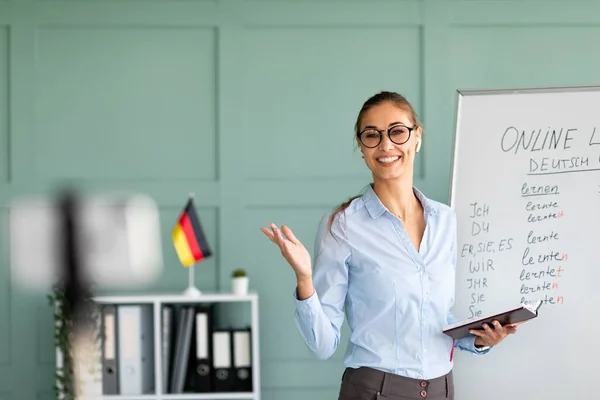 Online talenschool. Vriendelijke vrouwelijke leraar die Duitse les geeft op internet, smartphone gebruikt en grammatica uitlegt — Stockfoto