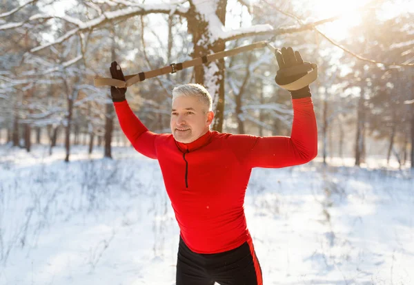 Спортивный пожилой человек делает упражнения с TRX фитнес-ремнями на открытом воздухе в снежный зимний день — стоковое фото