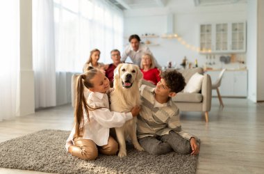 Tatlı Golden Retriever köpeğini kucaklayan sevimli çocuklar, yerde yan yana oturuyorlar, aileleri ve büyükanneleri arka planda.
