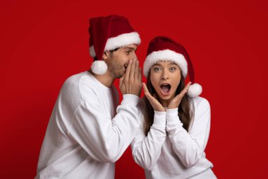 Noel Baba şapkalı genç adam heyecanlı kız arkadaşına Noel sırrını fısıldıyor.