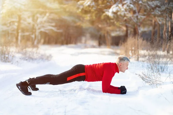 Outdoor winter sports and acclimation. Side view of mature sportsman standing in elbow plank pose at snowy forest — Stock Photo, Image