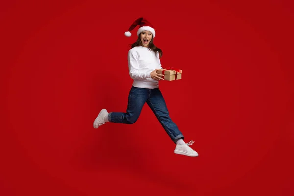 Mujer Milenial Positiva Usando Santa Sombrero Saltando En El Aire Con Caja De Regalo — Foto de Stock