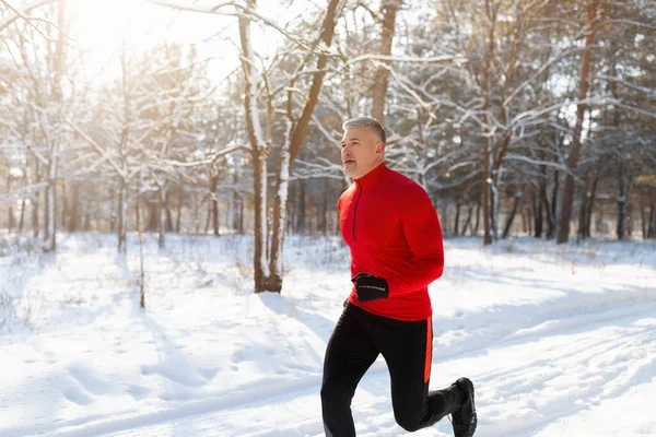 Hombre mayor atlético en ropa deportiva corriendo en el parque de invierno, trotando al aire libre en la mañana soleada helada, espacio de copia —  Fotos de Stock