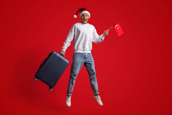 Turystyczne wycieczki. Mężczyzna w Santa kapelusz skacze z turecką flagą i walizką — Zdjęcie stockowe