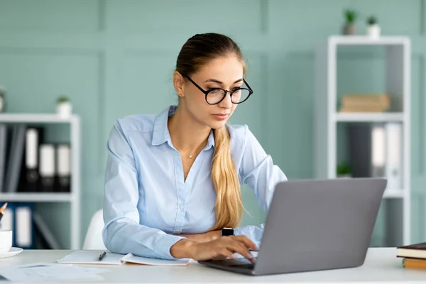 Årlig forretningskvinne som arbeider med en bærbar datamaskin ved skrivebordet, kvinnelig entreprenør som skriver på maskin – stockfoto