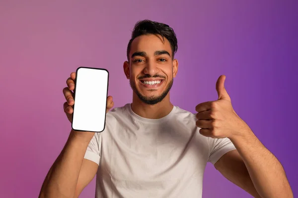 Homem árabe feliz mostrando gesto polegar para cima, demonstrando smartphone com tela vazia em luz de néon, mockup — Fotografia de Stock
