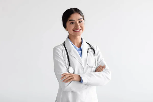 Feliz amigable joven mujer india atractiva médico en bata blanca con estetoscopio con brazos cruzados en el pecho —  Fotos de Stock