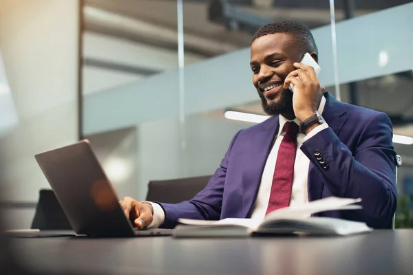 El empresario negro exitoso que trabaja en el ordenador portátil, que tiene conversación telefónica — Foto de Stock