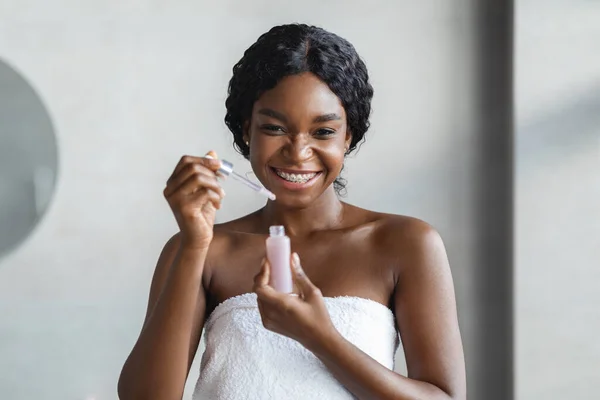 Wanita hitam muda yang bahagia memegang serum wajah. — Stok Foto