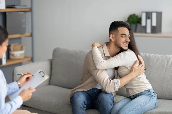 Amar a la pareja árabe abrazándose en la oficina de consejeros después de una terapia matrimonial exitosa, abrazando, celebrando el matrimonio salvado —  Fotos de Stock