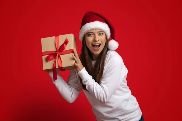 Bono de vacaciones. Mujer joven emocionada usando Santa Hat Holding envuelto caja de regalo — Foto de Stock