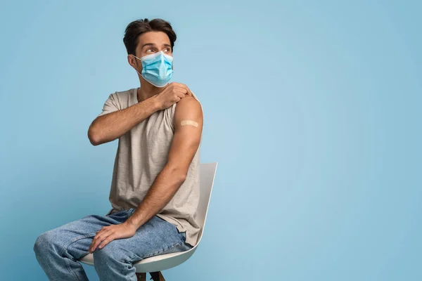 Millennial Guy in beschermende medische masker demonstreren arm met gips na vaccinatie — Stockfoto