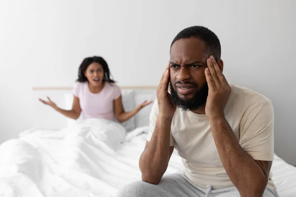 Αναστατωμένη θυμωμένη νεαρή Αφροαμερικανή γυναίκα να φωνάζει στον δυστυχισμένο σύζυγο στο λευκό κρεβάτι στο εσωτερικό της κρεβατοκάμαρας. — Φωτογραφία Αρχείου