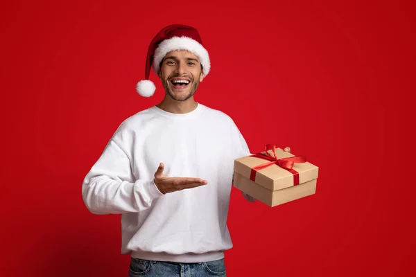 Hombre alegre con sombrero de Santa señalando la caja de regalo en su mano — Foto de Stock