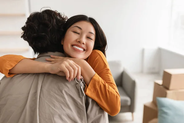 Young Asian lady hugging her husband and holding house key in their new apartment, copy space. Relocation concept — 图库照片