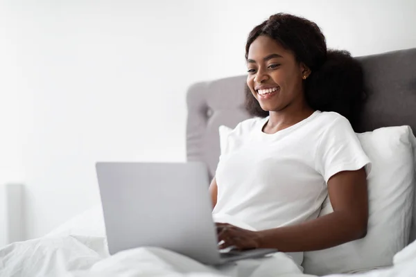 Junge schwarze Frau tippt auf Laptop, arbeitet im Bett — Stockfoto