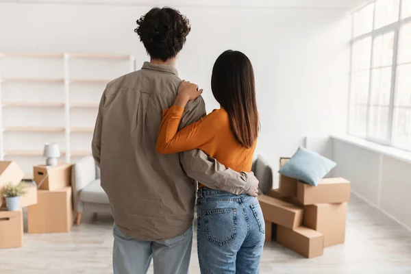 Vista trasera del joven con su novia abrazándose en la sala de estar de la nueva casa en el día de la mudanza. Reubicación —  Fotos de Stock