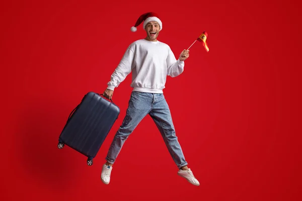 Happy Male Traveller Wearing Santa Hat Jumping With Spanish Flag And Suitcase — Stock Photo, Image