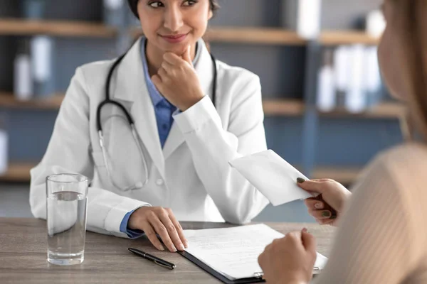 Cropped smiling young indian woman doctor in white coat with stethoscope takes money from patient — 图库照片