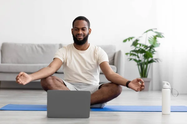 Tranquilo joven afroamericano con barba en ropa deportiva blanca con los ojos cerrados practicando yoga en posición de loto — Foto de Stock