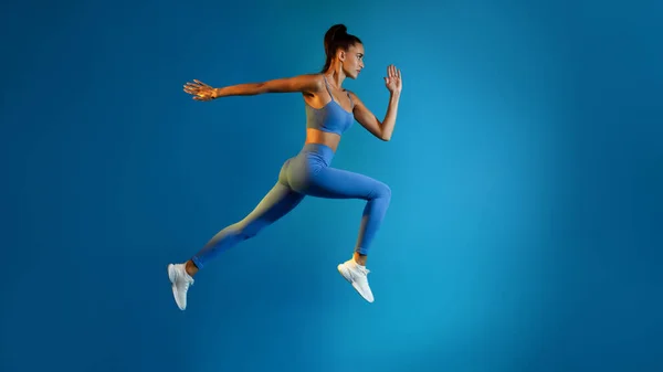 Bepaald jonge sportvrouw springen poseren in midden-lucht op blauwe achtergrond — Stockfoto