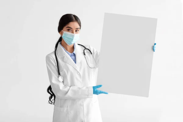 Femme thérapeute indienne millénaire sérieuse en manteau blanc avec stéthoscope en masque de protection, gants tiennent la bannière — Photo