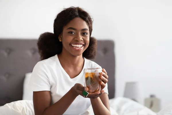Χαρούμενη Αφροαμερικανή κυρία που πίνει τσάι στο κρεβάτι. — Φωτογραφία Αρχείου