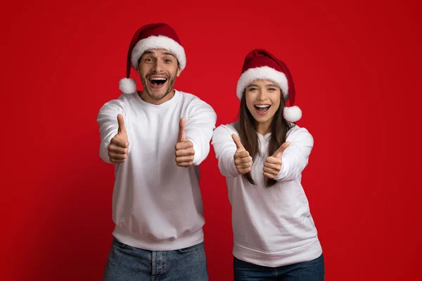 Портрет щасливої пари в капелюхах Санта показує великі пальці вгору на камеру — стокове фото